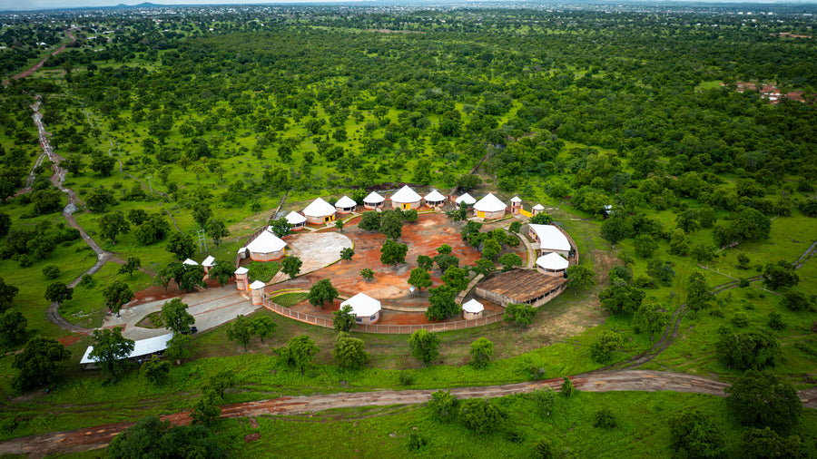 Aerial view of a circular cooperative compound of white-roofed buildings surrounded by green trees in northern Ghana.