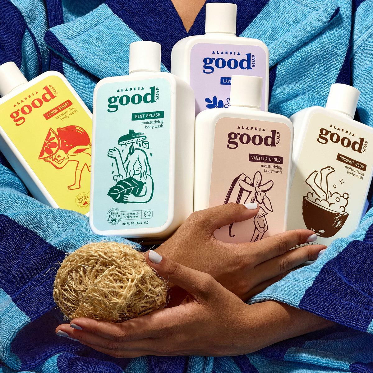 Five Good Soap body wash bottles in different scents held in an armful against a blue striped towel robe, with a natural loofah in hand.
