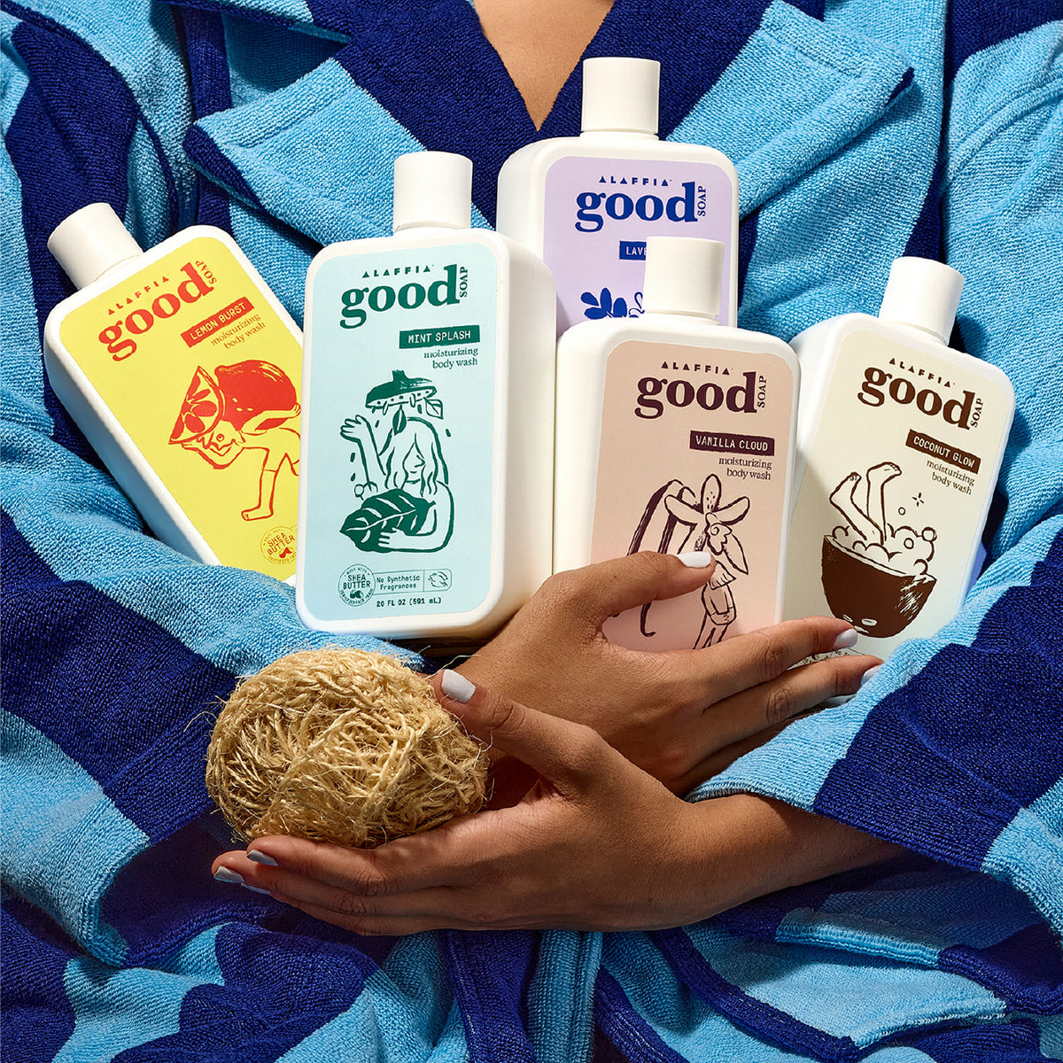 Good Soap body wash bottles in different scents: held in an armful against a blue striped robe, on a red-tiled shower shelf, and laid out on a bright blue surface.